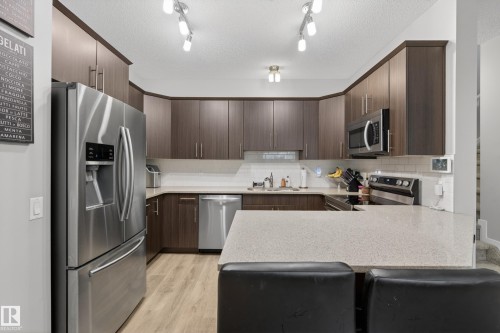 Contemporary kitchen featuring dark wood-finish cabinetry, stainless steel appliances, a light-toned countertop, subway tile backsplash, and wood-finish flooring - 70 James Crescent, St. Albert, AB 