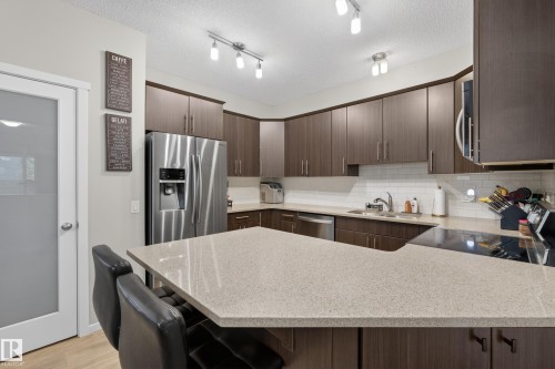 Kitchen featuring an expansive island with a light-toned countertop, wood-finish cabinetry, stainless steel appliances, and a white subway tile backsplash - 70 James Crescent, St. Albert, AB 