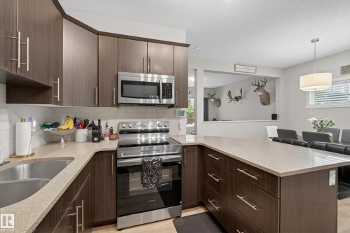 Kitchen featuring dark wood-finish cabinetry, stainless steel appliances, light-colored countertops, and a white subway tile backsplash - 70 James Crescent, St. Albert, AB 