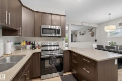 Kitchen featuring dark wood-finish cabinetry, stainless steel appliances, light-colored countertops, and a white subway tile backsplash - 
