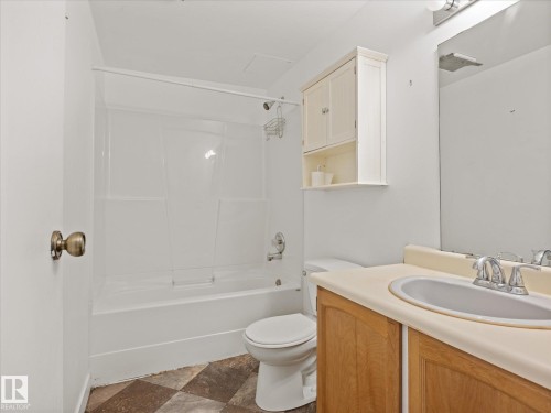 Bathroom featuring a full tub and shower combination with white surround, a single vanity with wood-finish cabinetry, a built-in mirror, and checkered flooring - 110 10139 117 Street, Edmonton, AB 