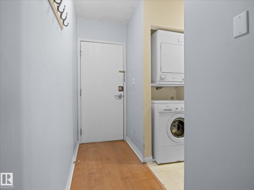 Hallway featuring wood-finish flooring, a white entry door, and a built-in coat rack - 110 10139 117 Street, Edmonton, AB 