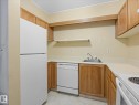 Compact kitchen featuring wood cabinetry, laminate countertops, a white refrigerator, a white dishwasher, and a white electric range - 110 10139 117 Street, Edmonton, AB 
