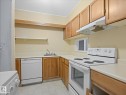 Kitchen featuring light wood cabinetry, a white electric range, a white dishwasher, a stainless steel sink, and light countertops - 110 10139 117 Street, Edmonton, AB 