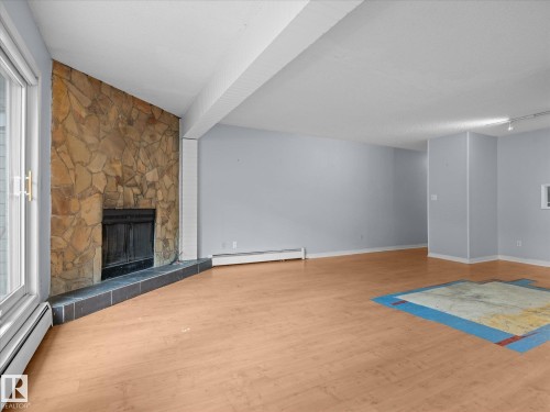 Spacious interior featuring a stone-clad fireplace with a slate hearth, wood-finish flooring, and light gray walls - 110 10139 117 Street, Edmonton, AB 