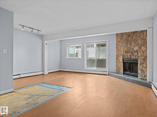 Living area featuring a stone-clad fireplace, wood-finish flooring, and track lighting - 110 10139 117 Street, Edmonton, AB 