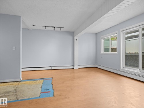 Bright interior space featuring light blue walls, two distinct window styles, and baseboard heating - 110 10139 117 Street, Edmonton, AB 