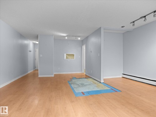 Spacious interior featuring wood-finish flooring, a neutral color palette, white baseboards, and ceiling-mounted track lighting - 110 10139 117 Street, Edmonton, AB 