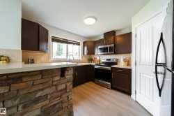 Kitchen featuring a stone-clad breakfast bar, white countertops, dark wood-finish cabinetry, stainless steel appliances, and wood-finish flooring - 