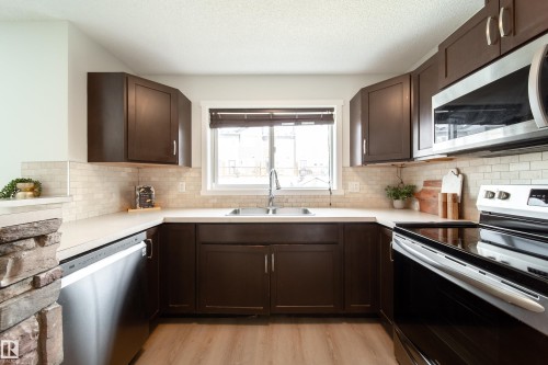 U-shaped kitchen featuring dark wood cabinetry, stainless steel appliances, light countertops, and a subway tile backsplash - 405 Simmonds Way, Leduc, AB 