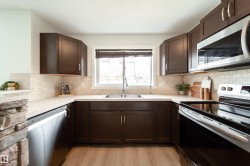 U-shaped kitchen featuring dark wood cabinetry, stainless steel appliances, light countertops, and a subway tile backsplash - 