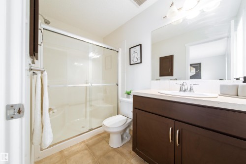 Bathroom featuring a dark wood-finish vanity with an integrated basin, chrome faucet, and a large wall-mounted mirror - 405 Simmonds Way, Leduc, AB 