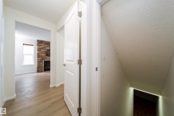 Hallway with light wood-finish flooring leading to a living area featuring a stone-clad fireplace and a window with horizontal blinds - 