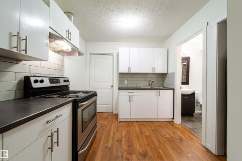 Kitchen featuring stainless steel range and oven, white cabinetry with brushed nickel hardware, dark countertops, and wood-finish flooring - 405 Simmonds Way, Leduc, AB 