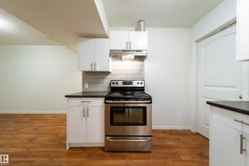 Kitchenette featuring a stainless steel range, white shaker-style cabinetry with chrome hardware, dark countertops, a white subway tile backsplash, and wood-finish flooring - 405 Simmonds Way, Leduc, AB 
