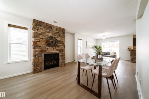 Stacked stone fireplace with a metal surround, wood-finish flooring, and white window blinds - 405 Simmonds Way, Leduc, AB 
