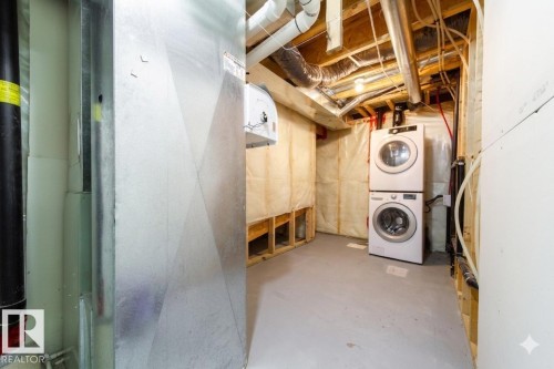 Dedicated laundry area featuring a stacked washer and dryer, exposed ceiling joists, substantial ductwork, and partial wall insulation - 405 Simmonds Way, Leduc, AB 