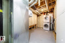 Dedicated laundry area featuring a stacked washer and dryer, exposed ceiling joists, substantial ductwork, and partial wall insulation - 