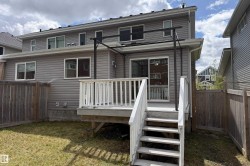 Rear exterior featuring a ground-level wood deck with stairs, a metal pergola frame, and grey siding - 