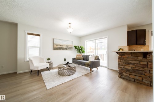 Open-concept living space featuring light wood-finish flooring, white walls, and a stone-clad kitchen island with a light-colored countertop - 405 Simmonds Way, Leduc, AB 