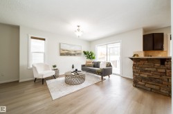 Open-concept living space featuring light wood-finish flooring, white walls, and a stone-clad kitchen island with a light-colored countertop - 