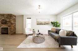Spacious living area featuring light wood-finish flooring, a stacked stone fireplace, a large sliding glass door, a single window, and a ceiling-mounted light fixture - 