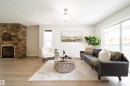 Spacious living area featuring light wood-finish flooring, a stacked stone fireplace, a large sliding glass door, a single window, and a ceiling-mounted light fixture - 405 Simmonds Way, Leduc, AB 