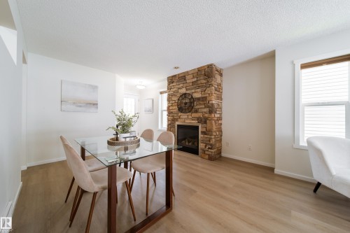 This living area features a stone-clad fireplace with an integrated firebox, wood-finish flooring, and white walls - 405 Simmonds Way, Leduc, AB 