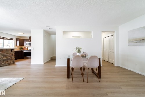 Light wood-finish flooring extends through this open-concept space, featuring white walls and a kitchen with dark cabinetry and stainless steel appliances - 405 Simmonds Way, Leduc, AB 