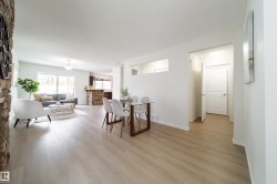 Open-concept living space with light wood-finish flooring, a stone-clad accent wall, a dining area, a living area, and a kitchen visible in the background - 