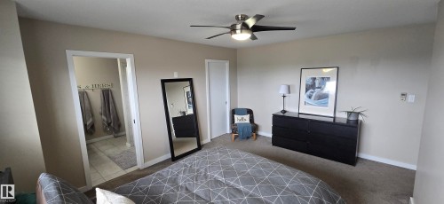 Carpeted bedroom featuring neutral wall tones, a ceiling fan with integrated lighting, and a doorway revealing a tiled bathroom space - 4234 46 Street, Vegreville, AB - Indoor Photo Showing Bedroom
