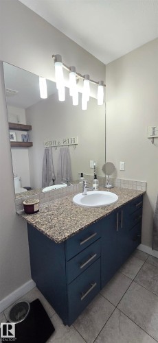 Bathroom vanity featuring a vessel sink, speckled countertop, and dark blue cabinetry with brushed nickel hardware - 4234 46 Street, Vegreville, AB - Indoor Photo Showing Bathroom