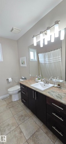 Bathroom featuring a dark wood-finish vanity with a drop-in sink, a stone-finish countertop, and a large mirror - 4234 46 Street, Vegreville, AB - Indoor Photo Showing Bathroom