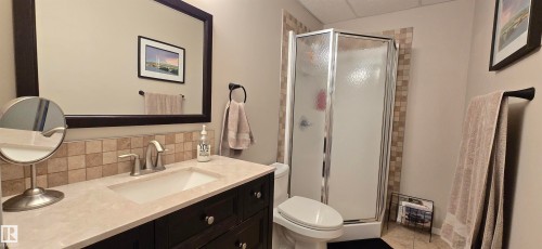 Bathroom featuring a shower enclosure, vanity with integrated sink, tiled backsplash, and a framed mirror - 4234 46 Street, Vegreville, AB - Indoor Photo Showing Bathroom