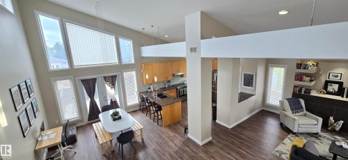 Vaulted ceiling living area featuring wood-finish flooring, a kitchen with light wood cabinetry, a central island with bar seating, and a dining space with double glass doors - 4234 46 Street, Vegreville, AB - Indoor