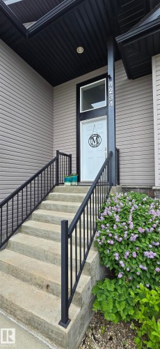 Exterior entry featuring a white paneled door with an overhead transom window, concrete steps, black metal railings, and a prominent house number - 4234 46 Street, Vegreville, AB - Outdoor With Exterior