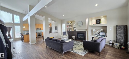 Open-concept living area featuring wood-finish flooring, a contemporary fireplace with dark tile surround and mantel, and built-in shelving with integrated lighting - 4234 46 Street, Vegreville, AB - Indoor Photo Showing Living Room With Fireplace
