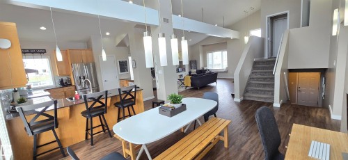 Open-concept living area featuring wood-finish flooring, vaulted ceilings, and a kitchen with light wood cabinetry and stainless steel appliances - 4234 46 Street, Vegreville, AB - Indoor Photo Showing Dining Room