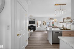 Open-concept living space featuring wood-finish flooring throughout, a kitchen island with a built-in dishwasher, a brass-finish faucet, and pendant lighting - 