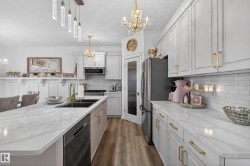 Contemporary kitchen featuring white cabinetry with gold-tone hardware, wood-finish flooring, and white countertops with subtle veining - 