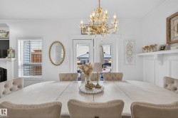 Dining area featuring a white wood-finish table with upholstered chairs, a gold-toned chandelier, and a white mantelpiece - 