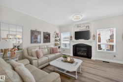 Living room featuring wood-finish flooring and a central fireplace with a dark stone-look surround and white mantle - 