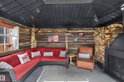 Covered outdoor living space featuring a dark metal gazebo roof, wood-planked walls, and a built-in outdoor fireplace - 