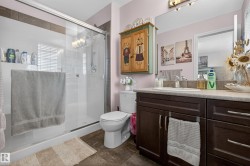Bathroom featuring a glass-enclosed shower with a built-in shelf, a white toilet, and a vanity with a light-colored countertop and dark wood-finish cabinetry - 