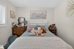 Neutral-toned interior room featuring a window with white blinds, a white-painted bed frame, and a dark wood-finish dresser with white knobs - 