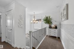 Carpeted hallway featuring white wainscoting and a staircase with black metal balusters - 