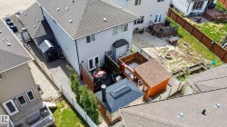 Rear exterior featuring a spacious composite deck, a covered hot tub structure, a separate shed with a pitched roof, a paved side yard, and a fenced perimeter - 