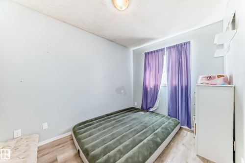 Bright interior room featuring wood-finish flooring, light blue walls, and a window with purple drapes - 10017 153 Street, Edmonton, AB - Indoor Photo Showing Bedroom