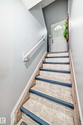 Staircase featuring tiled treads with blue nosing and a white handrail, leading to a white entry door with a decorative glass insert - 10017 153 Street, Edmonton, AB - Indoor Photo Showing Other Room