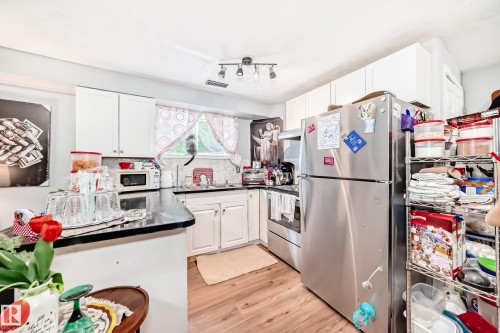 Kitchen featuring wood-finish flooring, white cabinetry, dark countertops, a tile backsplash, and a stainless steel refrigerator - 10017 153 Street, Edmonton, AB - Indoor Photo Showing Kitchen